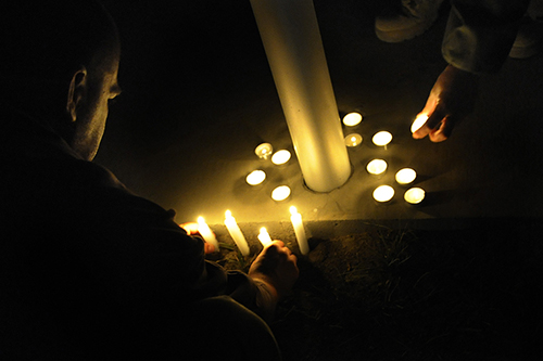 An image of persons leaving lit candles need the base of a memorial for the lives lost at the Kabul Airport